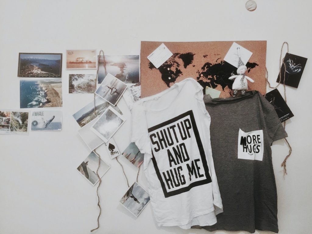 Fotos, camisetas e lembranças de viagem aparecem na imagem decorando uma parede branca.