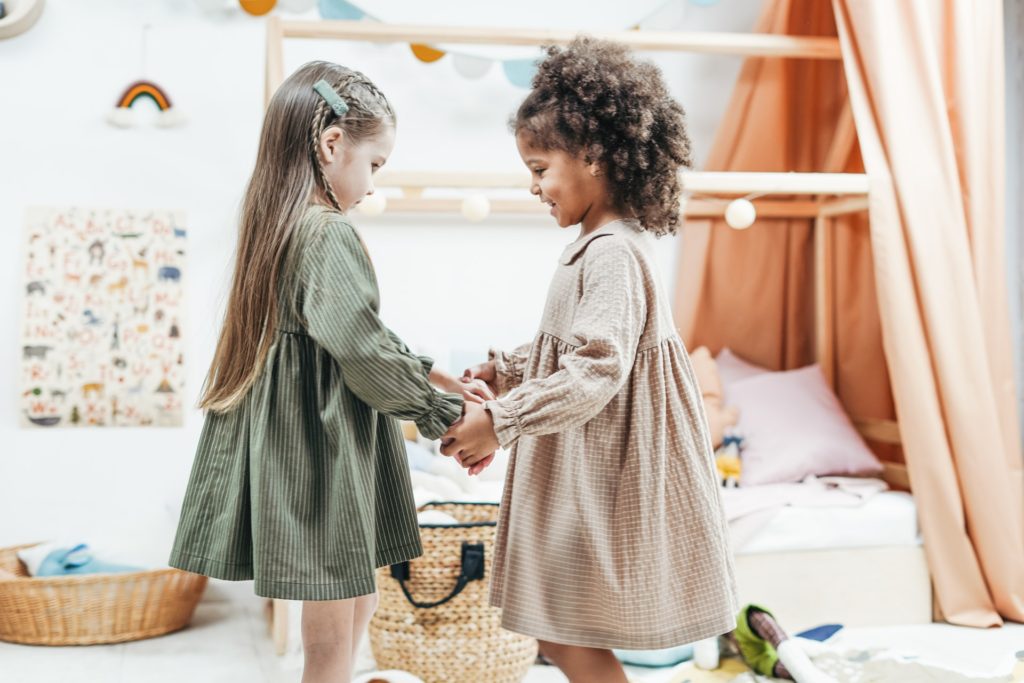 Uma menina branca e uma menina negra brincam juntas de mãos dadas, imagem representa a importância de uma educação com diversidade.