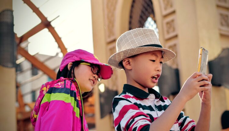Duas crianças viajando, um menino e uma menina olham para o celular como se estivessem olhando para uma foto recém tirada.