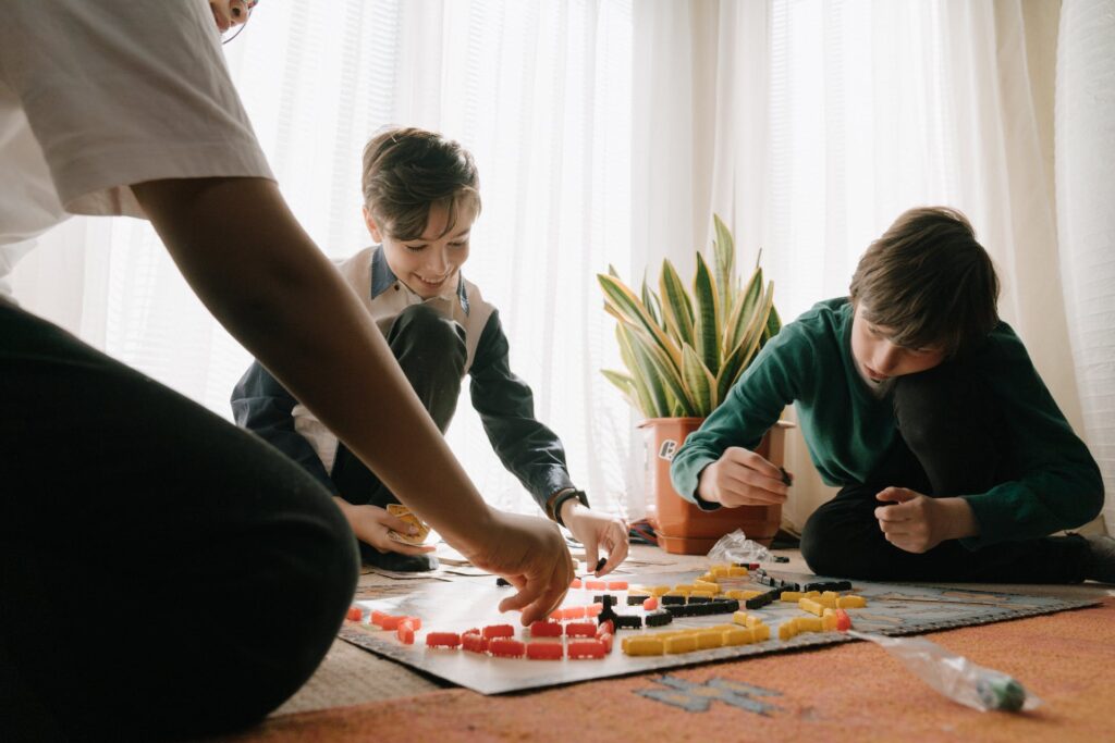 Crianças brancas jogando um jogo de tabuleiro sentadas no chão.