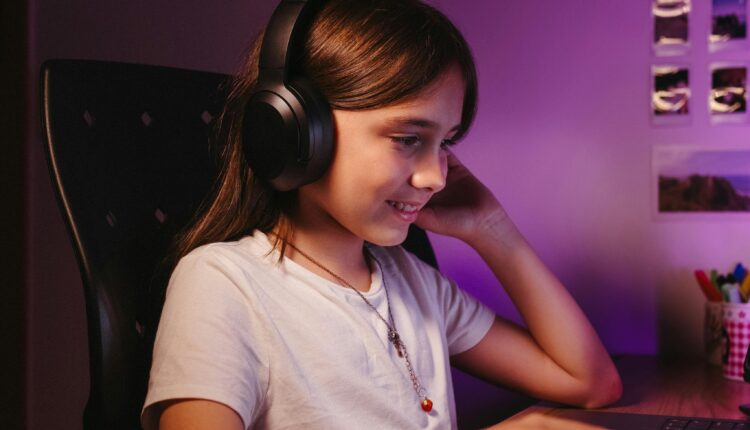 Criança escuta um podcast em seu headphone sentada em frente ao computador.
